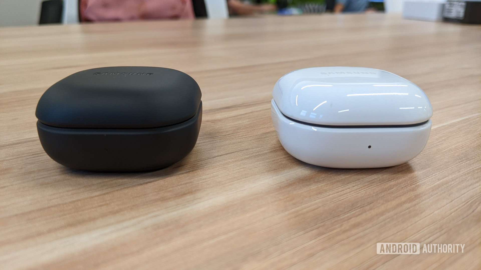The Samsung Galaxy Buds 2 Pro case in graphite next to the Buds 2 case in white on a wooden table seen from the front.