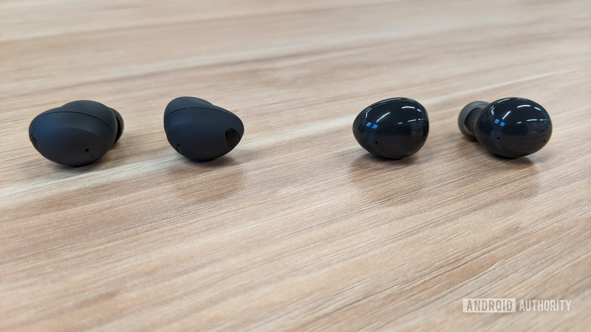 The Samsung Galaxy Buds 2 Pro in graphite outside of the case next to the Buds 2 in graphite outside of their cases sitting on a table seen from the front.