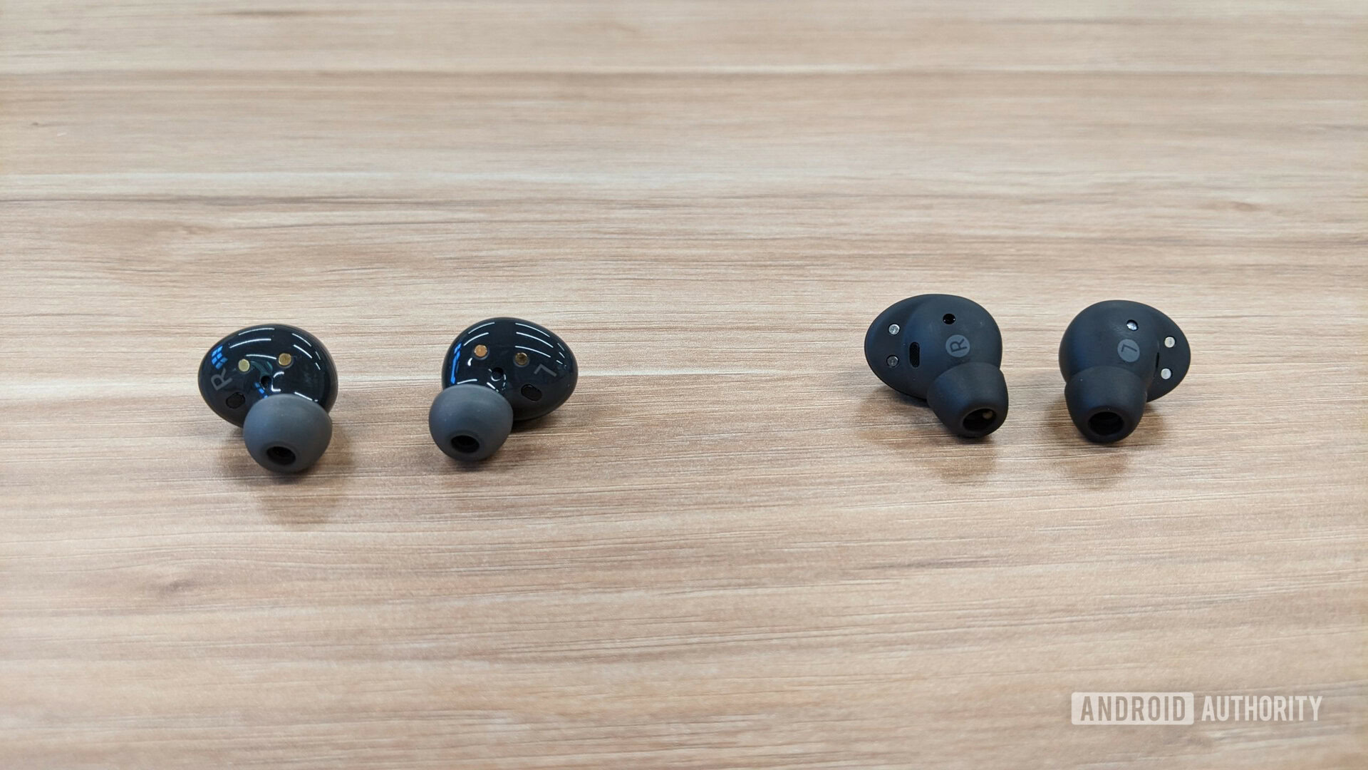 The Samsung Galaxy Buds 2 Pro in graphite outside of the case next to the Buds 2 in graphite outside of their cases sitting on a table seen from the back.