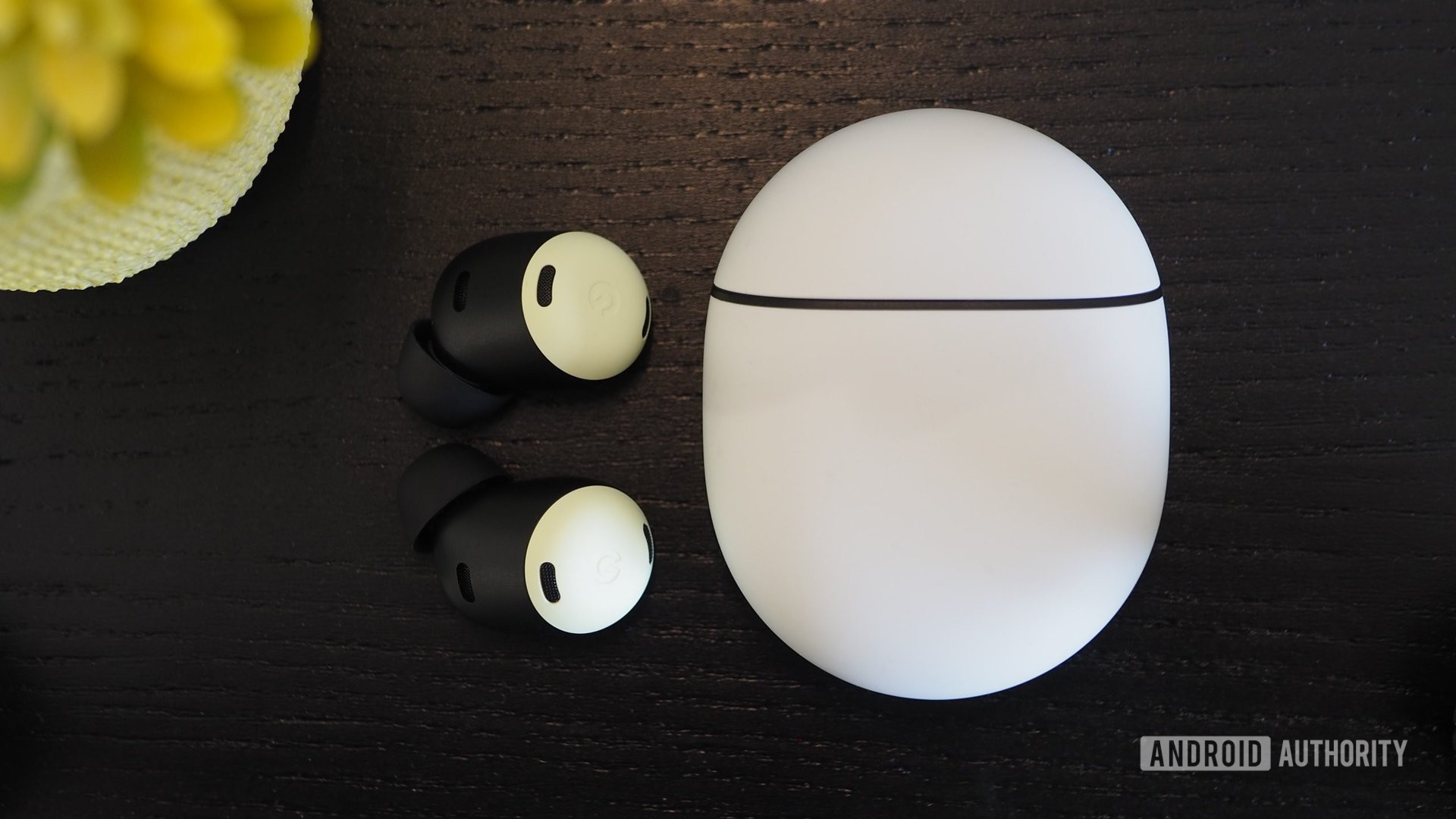 A pair of Google Pixe Buds Pro outside their closed case lying on a wooden table.