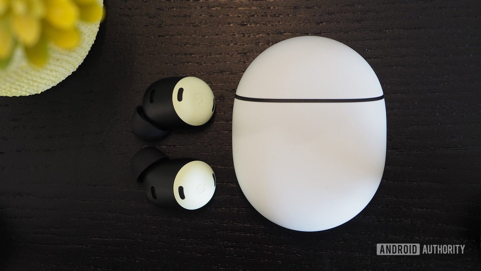 A pair of Google Pixe Buds Pro out of the sealed case lying on a wooden table.