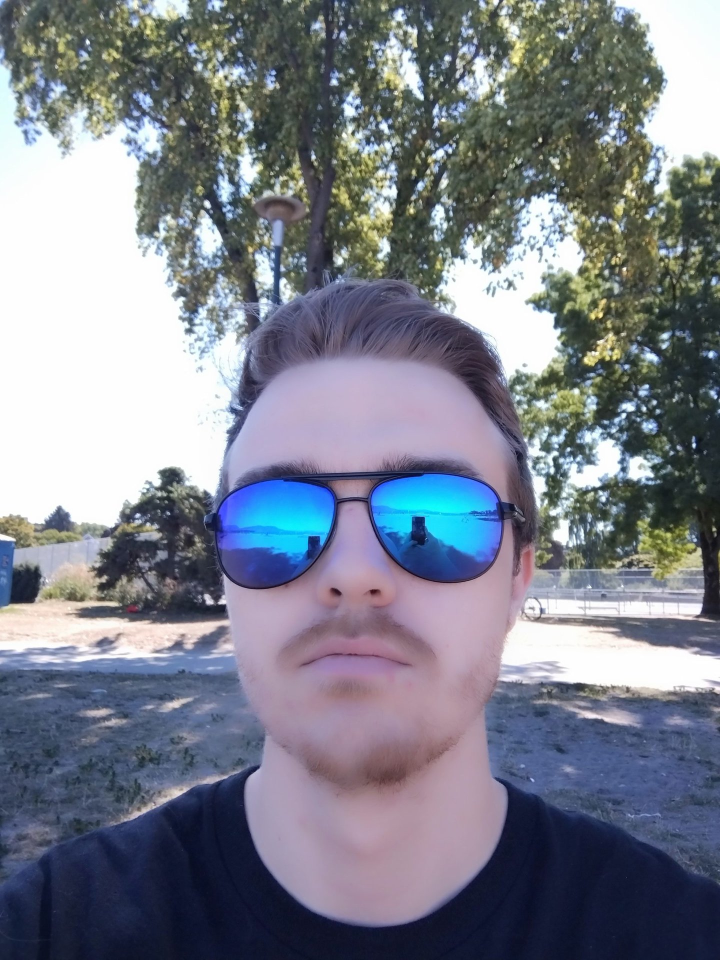 portrait selfie of a man with short hair in a black t-shirt wearing mirrored blue aviator shades with beauty filter