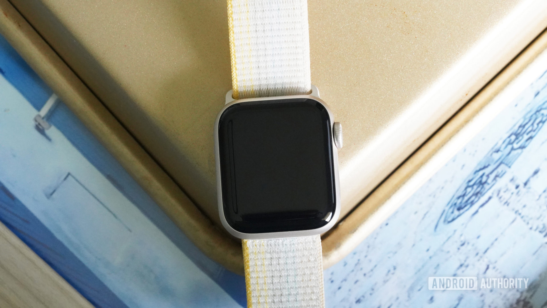 An Apple Watch rests on a gold and blue surface with the screen off. 