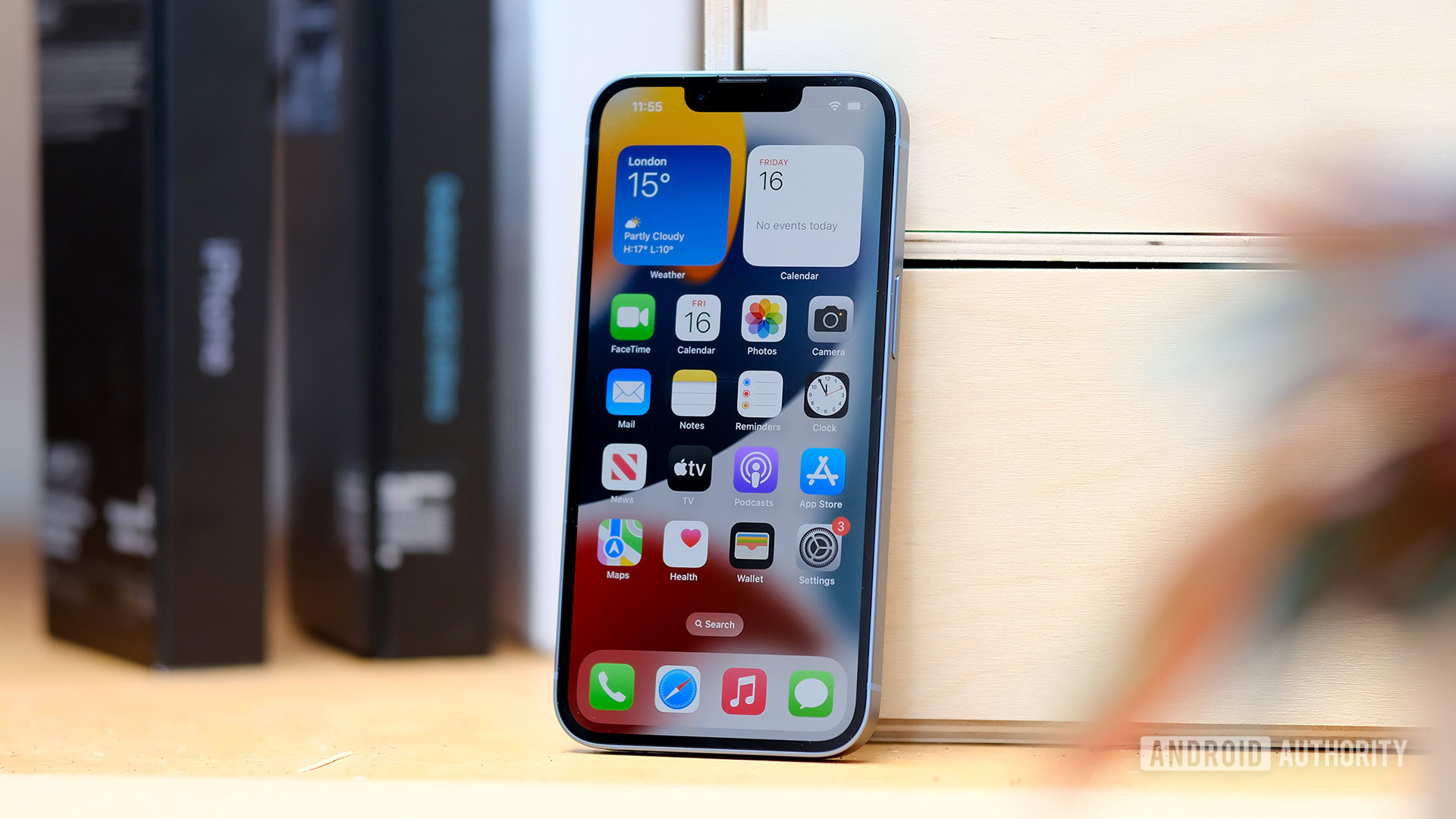 An Apple iPhone 14 seen from the front resting against a chest of drawers.