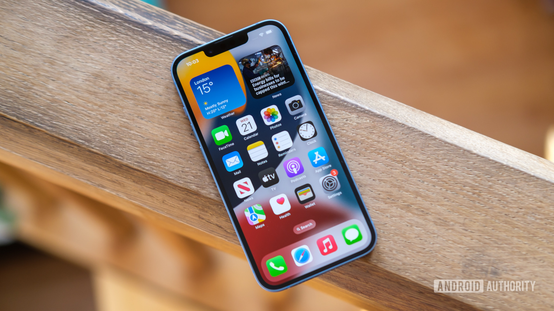 An Apple iPhone 14 showing its homescreen resting face up on a wooden railing.