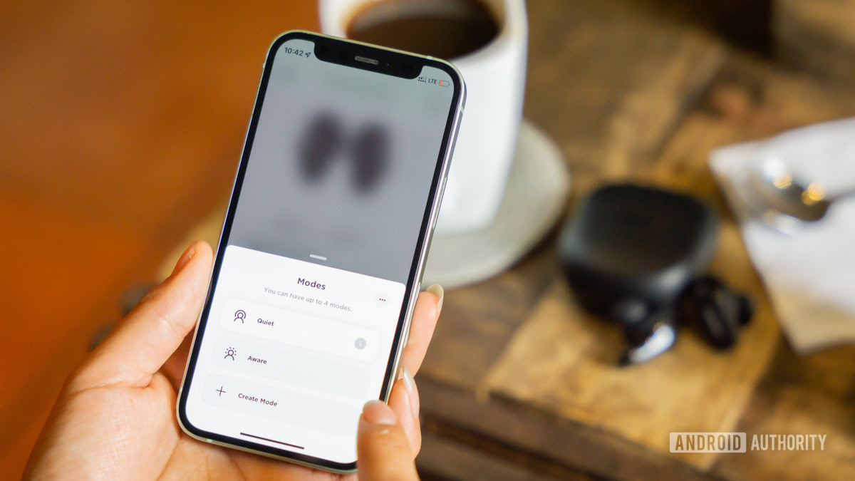 Bose QuietComfort Earbuds 2 in the background with a smartphone choosing Modes in the foreground.