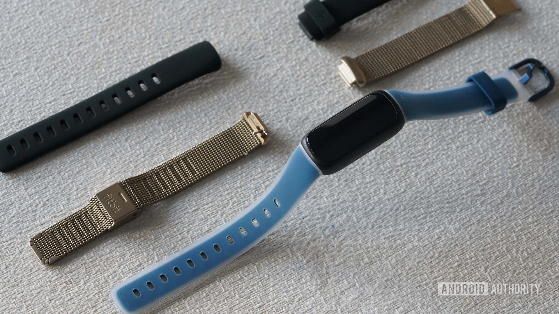 A Fitbit Inspire 3 and two alternative bands rest on a white fabric surface.