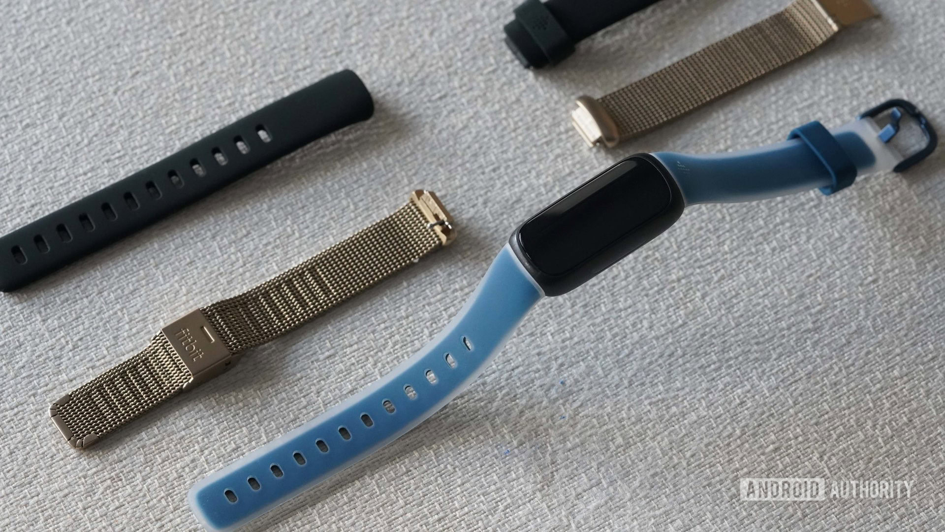 Un Fitbit Inspire 3 et deux bracelets alternatifs reposent sur une surface en tissu blanc.