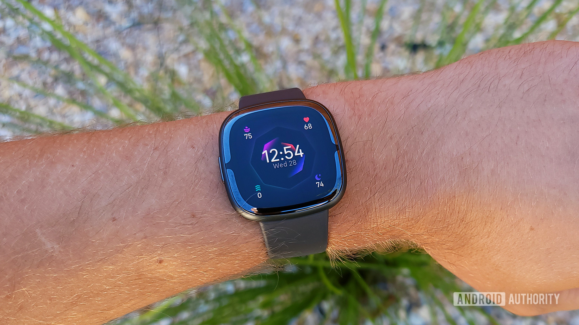 A Fitbit Sense 2 on a user's wrist displays the default watch face.