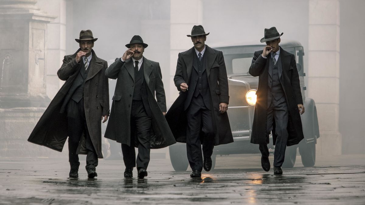 Four men in suits and trench coats walk down a rainy street in Gun City - best gangster movies on netflix