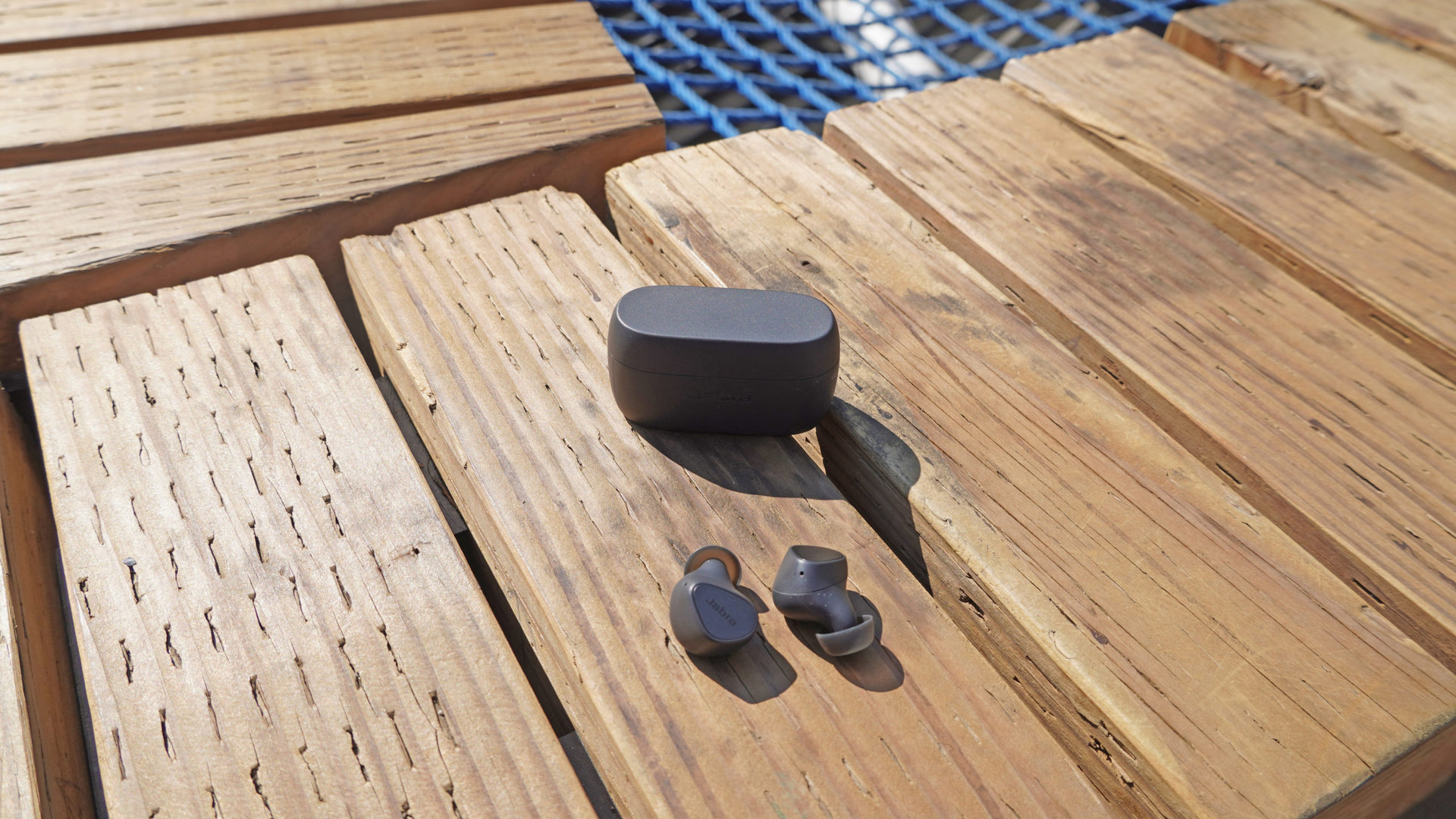The Jabra Elite 3 earbuds sitting next to their case outdoors on a wooden bench.
