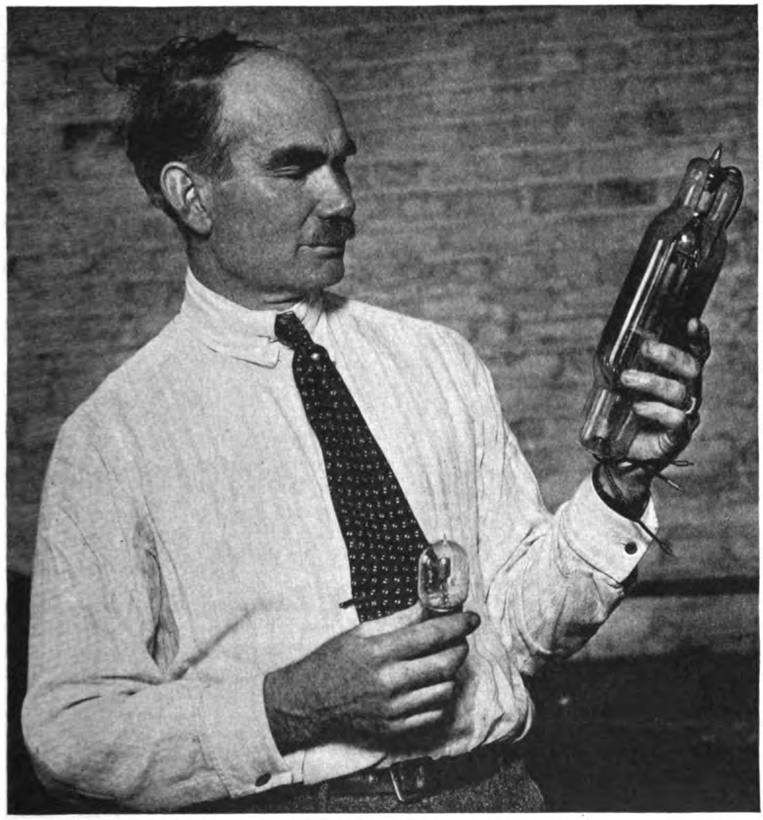 A black and white photo of Lee De Forest with holding an audion tube in each hand.