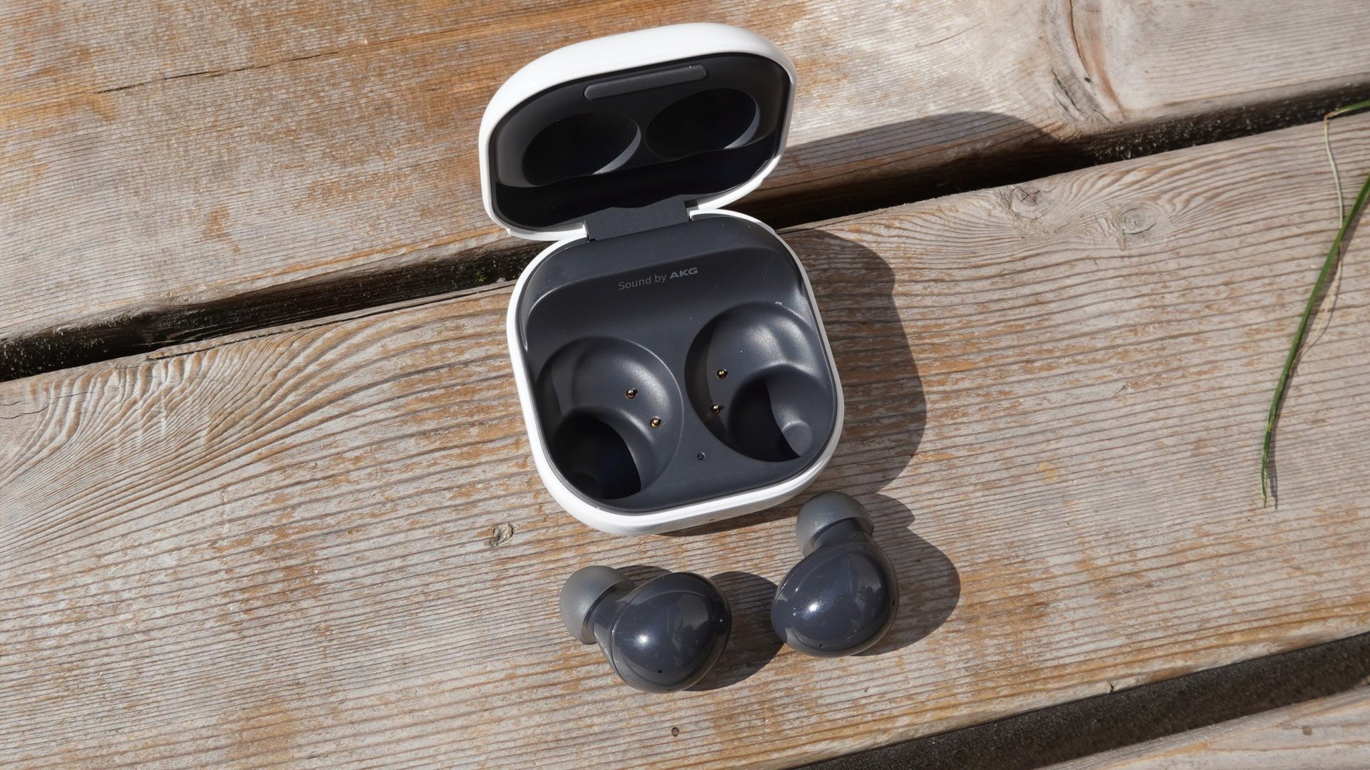 The Galaxy Buds 2 next to their case sitting on a wooden bench outdoors.