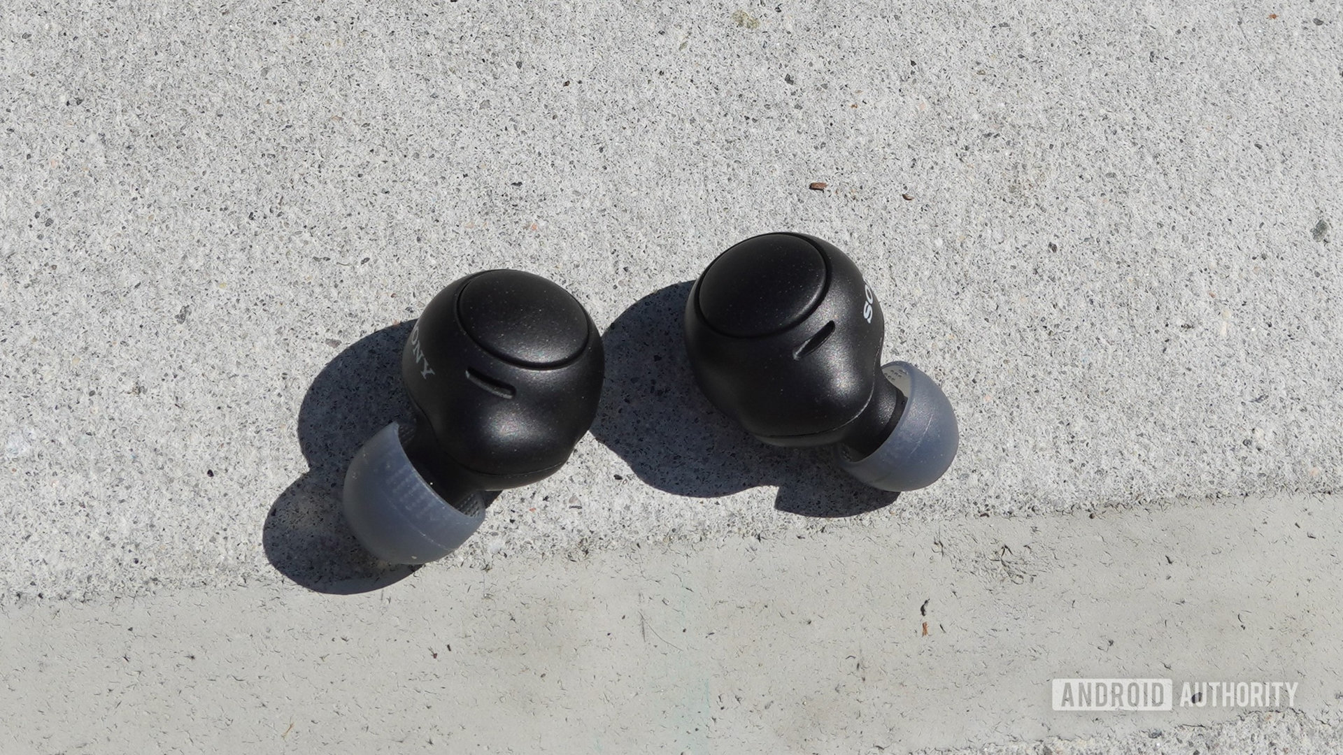 The Sony WF-C500 earbuds lying outside on concrete.