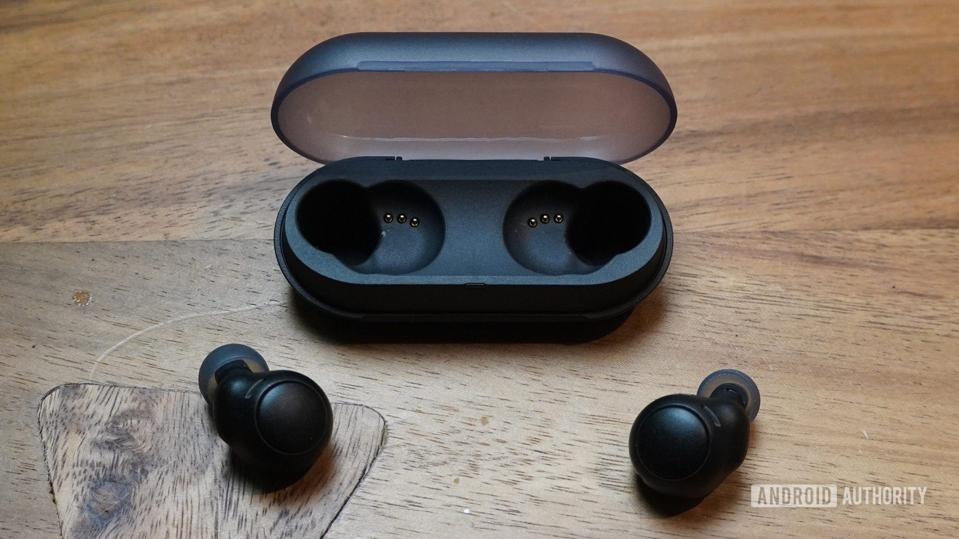 The Sony WF-C500 earbuds lying outside of their case next to a smartphone phone on a table.