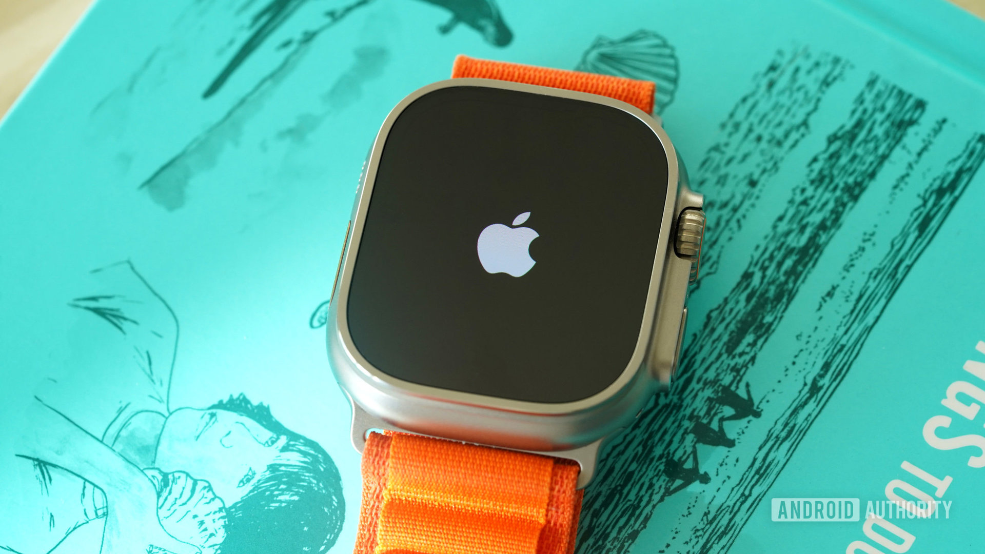 An Apple Watch Ultra rests on a teal book, displaying the Apple logo.