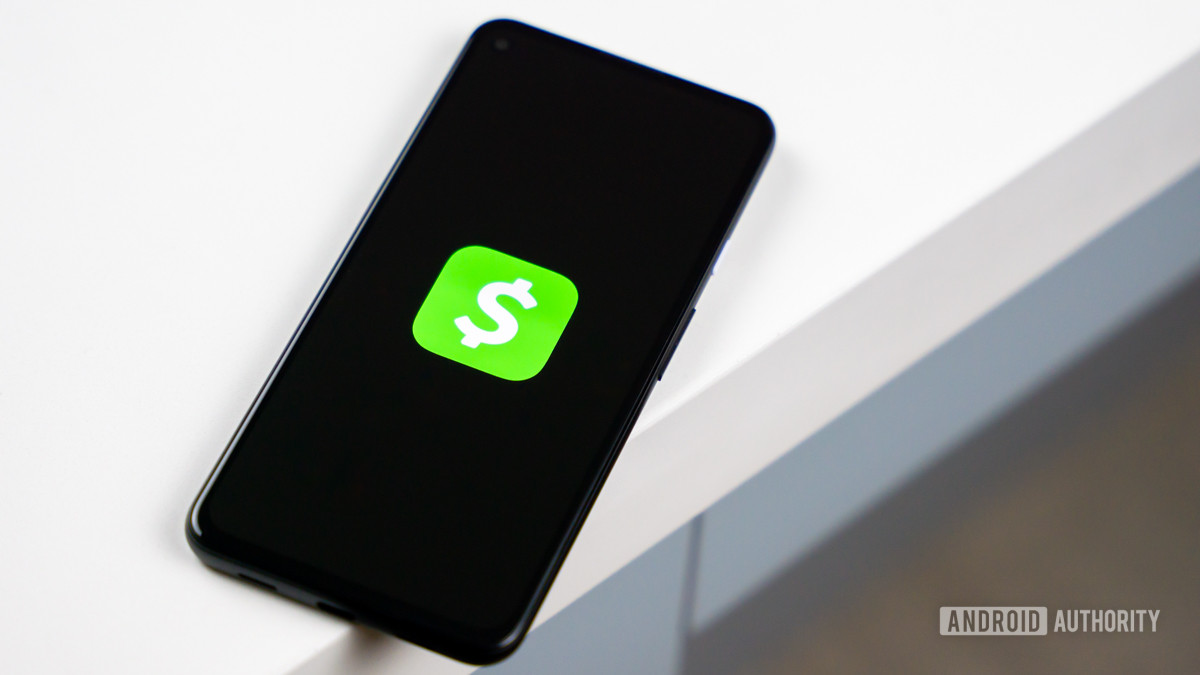 A stock photo of the Cash App logo shown on a smartphone sitting on the edge of white table.