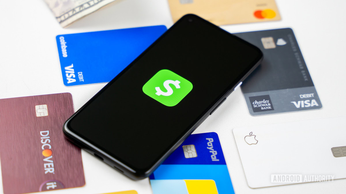 A stock photo of a smartphone showing the Cash App logo on its screen. It lies on top of some credit and debit cards.