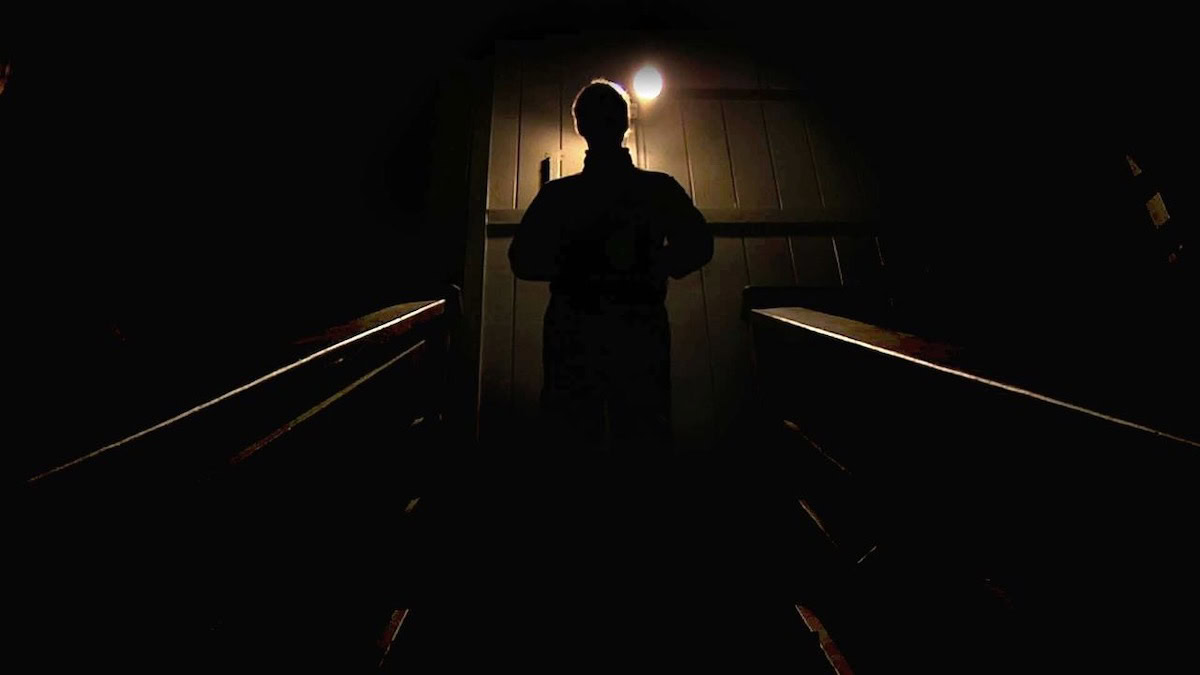 A man stands at the top of a staircase, hidden in shadow in Creep - best thriller movies on Netflix