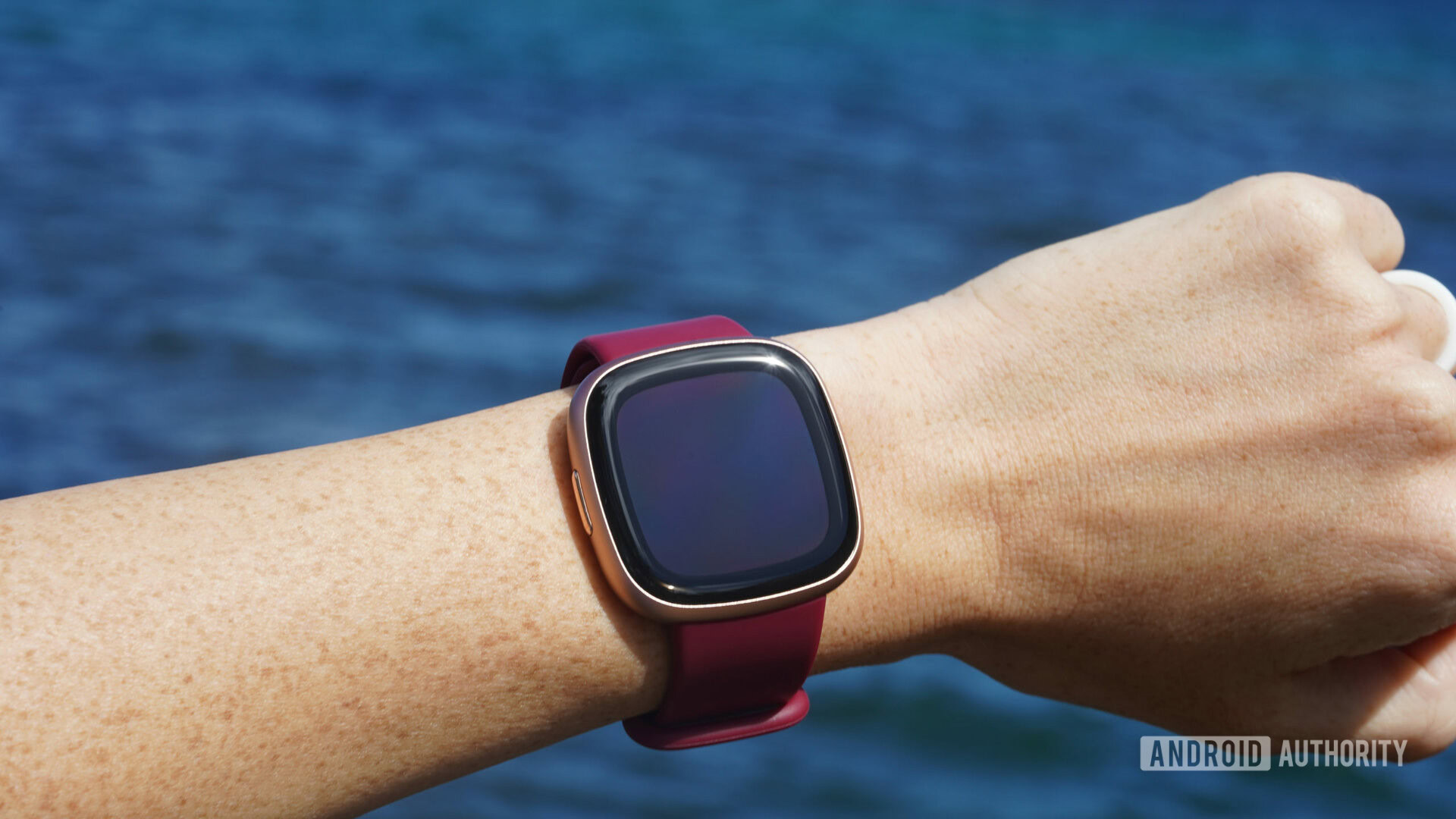 A Fitbit Versa 4 on a user's wrist displays a blank screen.