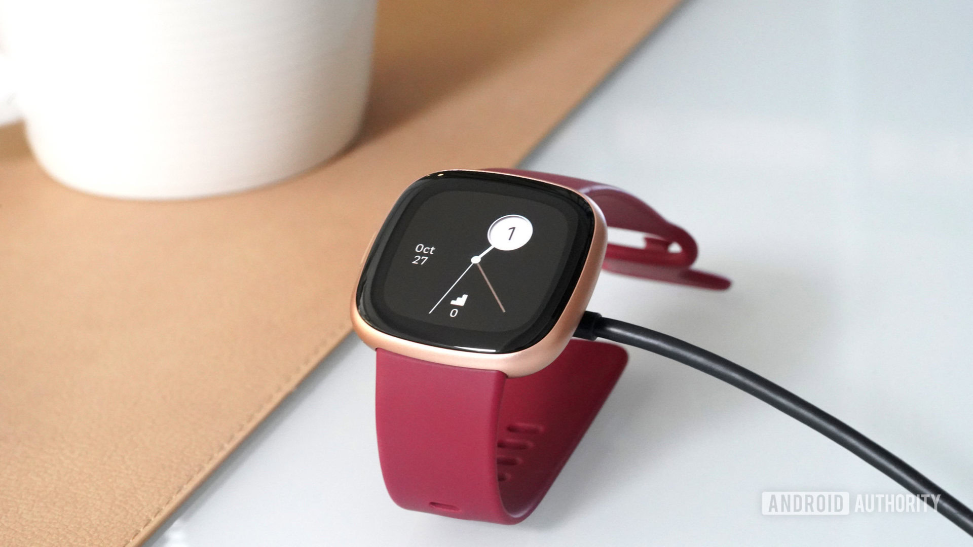 A Fitbit Versa 4 charges on a user's desk.