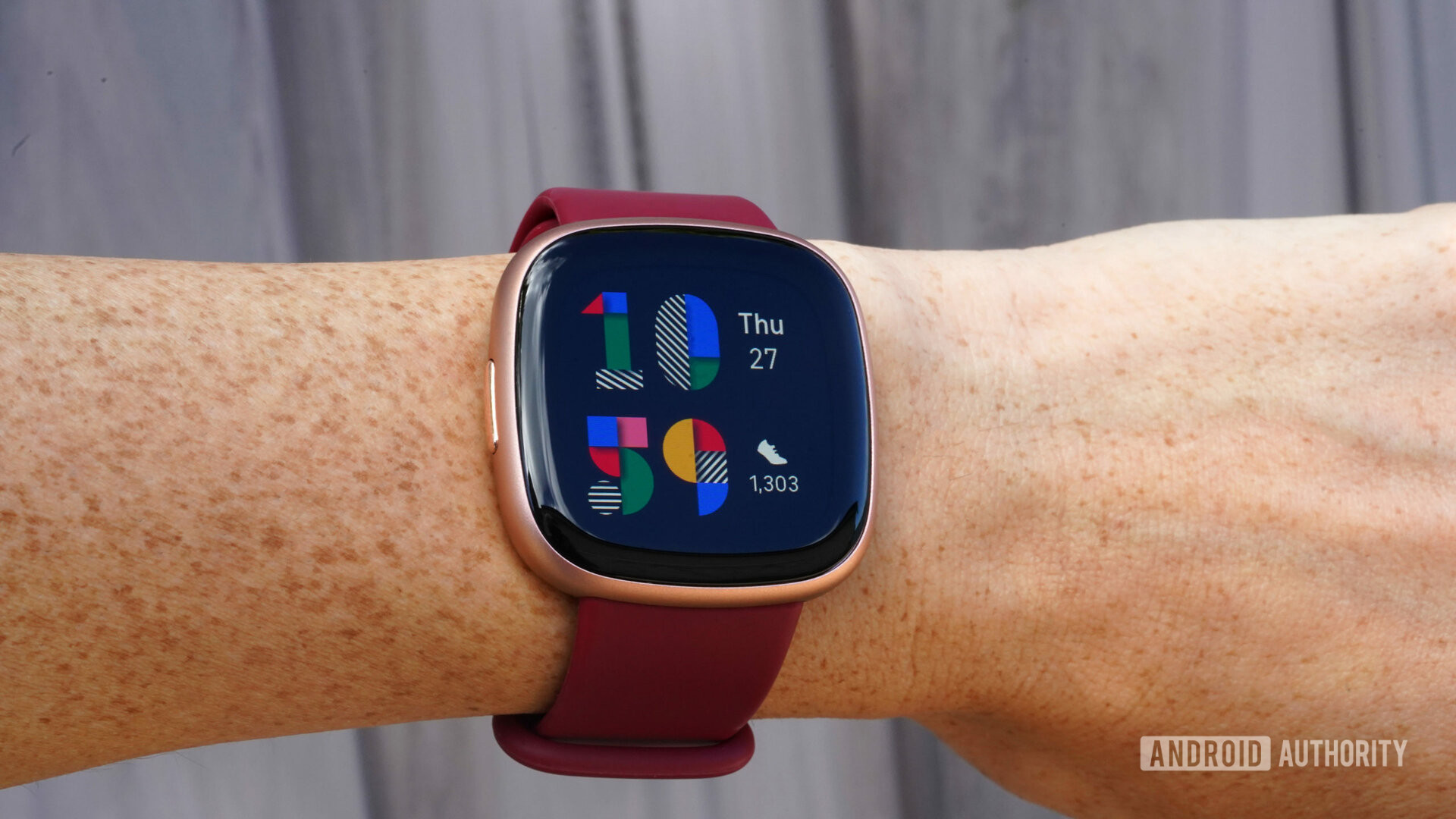 Fitbit Versa 4 di pergelangan tangan pengguna menampilkan tampilan jam Playpen yang berwarna-warni.