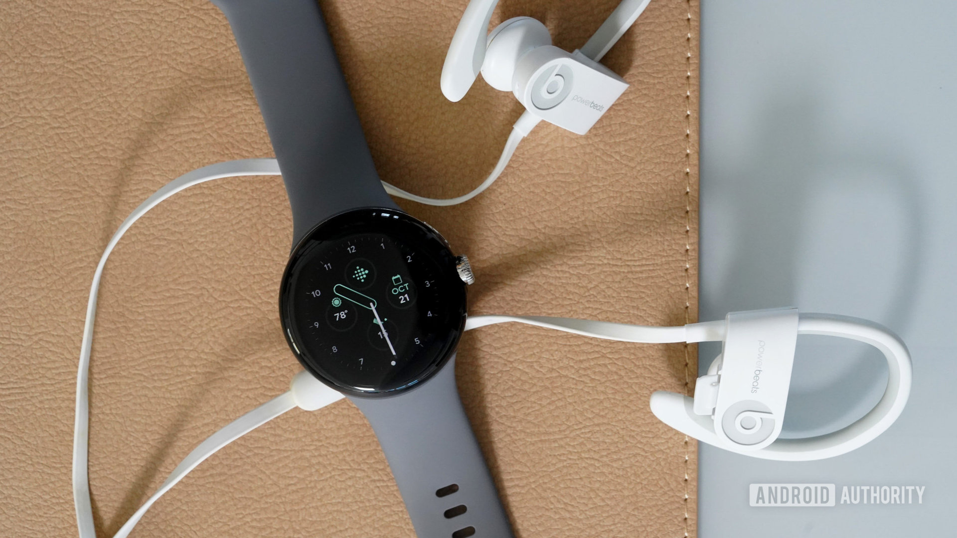 A Google Pixel Watch rests on a desk along side a pair of Bluetooth headphones.