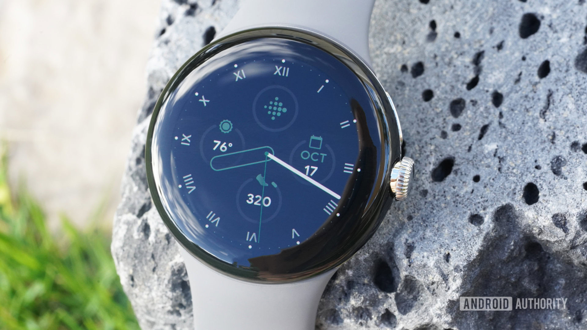 A Google Pixel Watch rests on lava rock displaying the watch face.