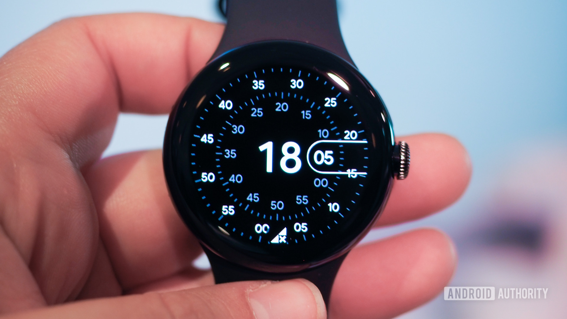 A user holds a Google Pixel Watch displaying a watch face.