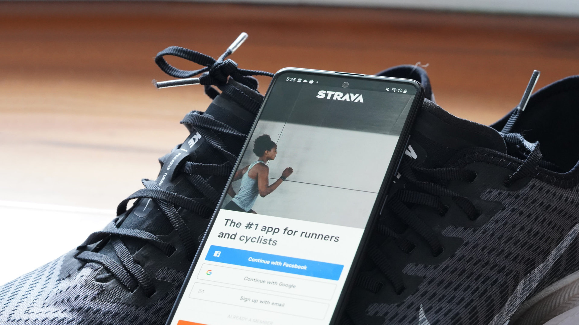 A Galaxy A51 resting on a running sneakers displays the Strava signup screen.