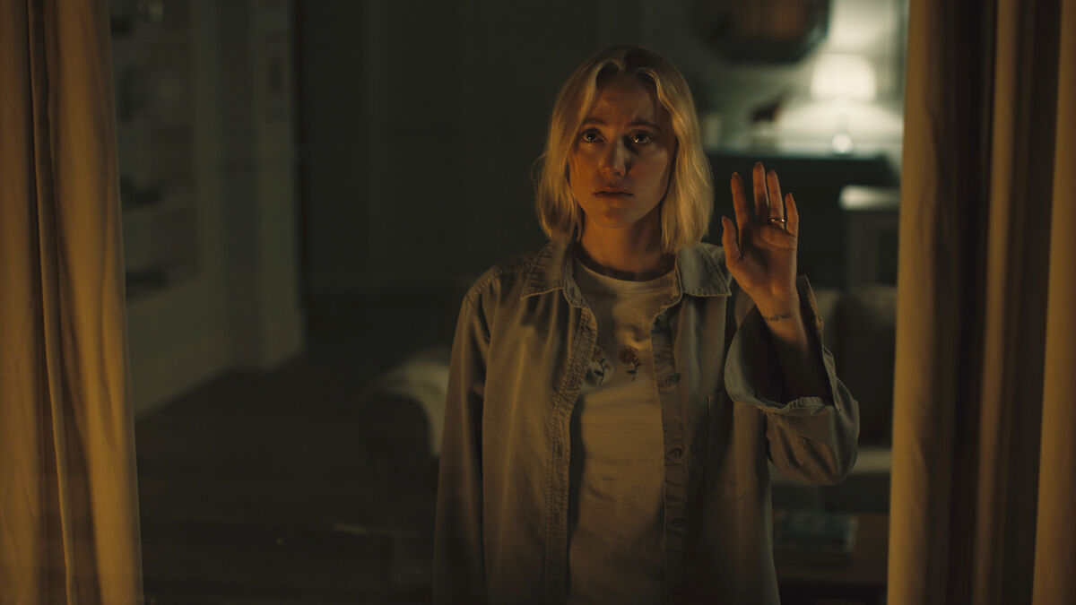 A woman waves out her window at night in Watcher - best horror films of 2022