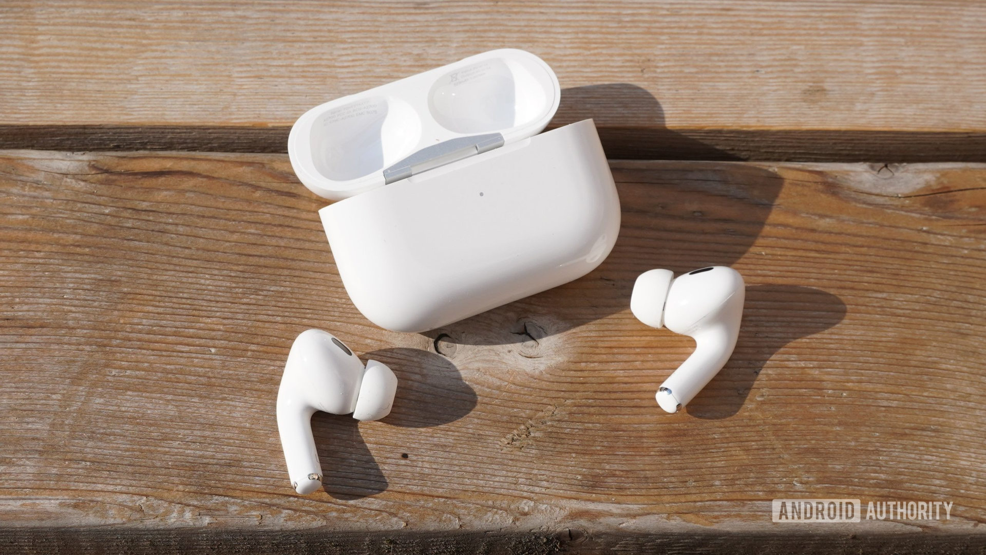 The AirPods Pro 2 sitting outside their case on a wooden surface with the case nearby.