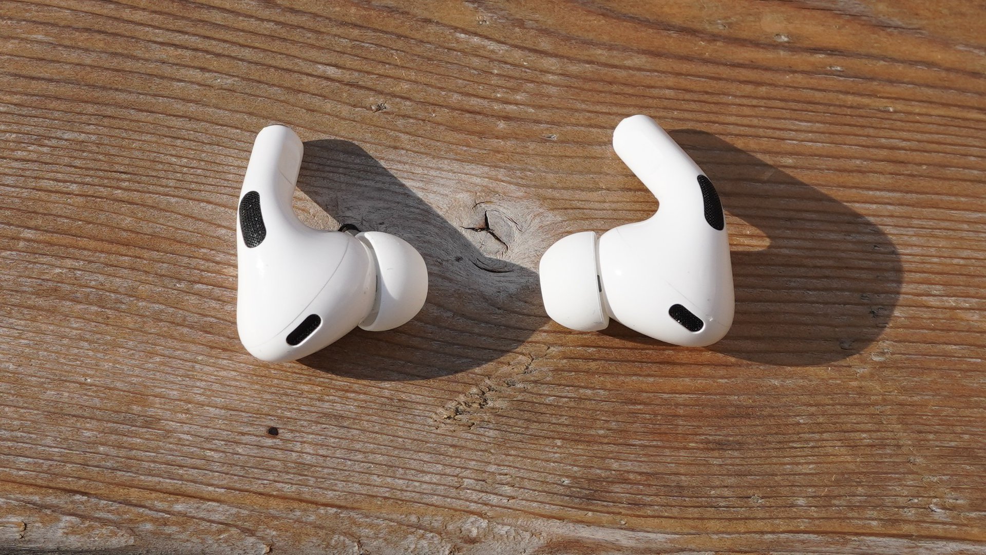 The AirPods Pro 2 sitting outside their case on a wooden surface.