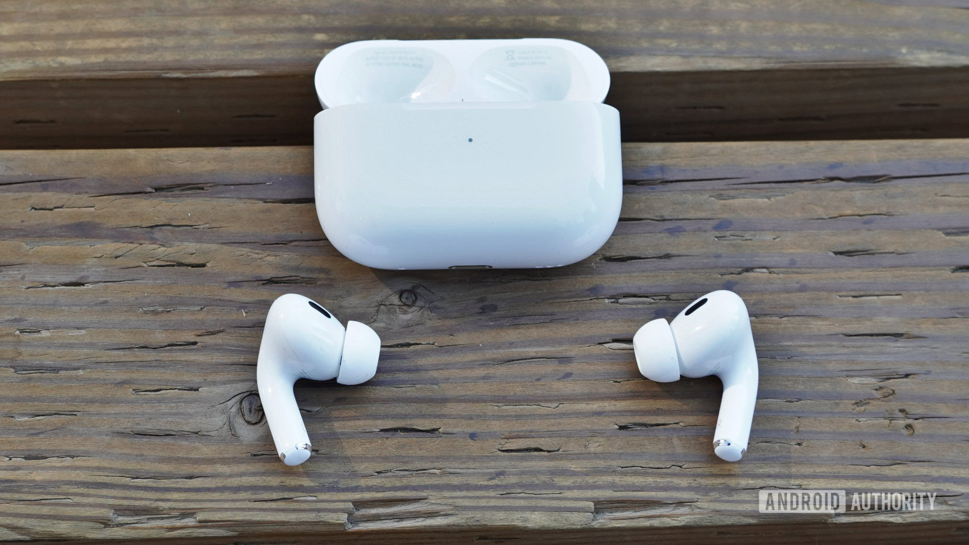 The AirPods Pro 2 sitting outside their case on a wooden surface with the case nearby.