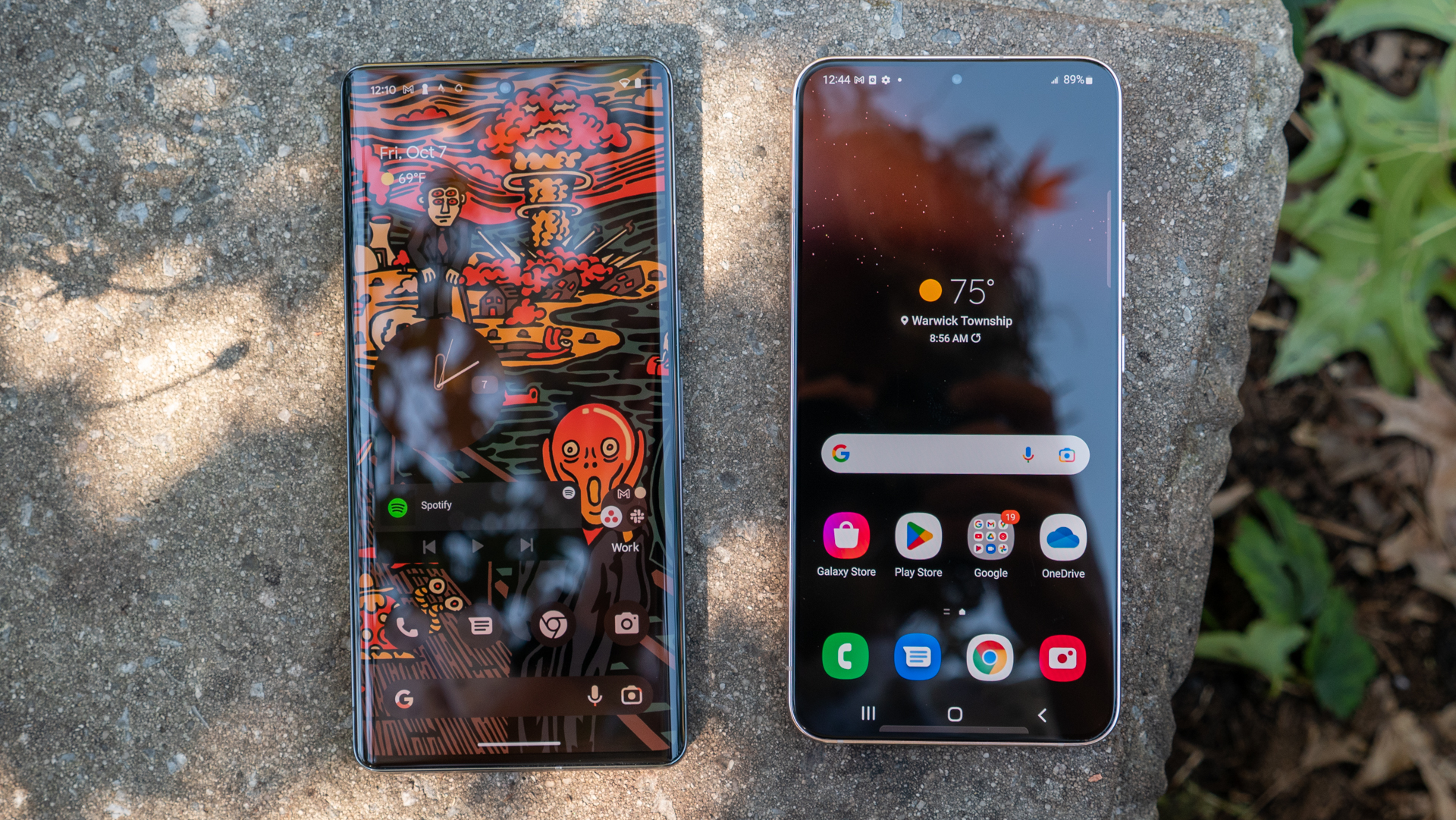 A Ggoogle Pixel 7Ppro next to a Samsung Galaxy S22 Plus shwing their home screens. Both rest on a concrete block outdoors.