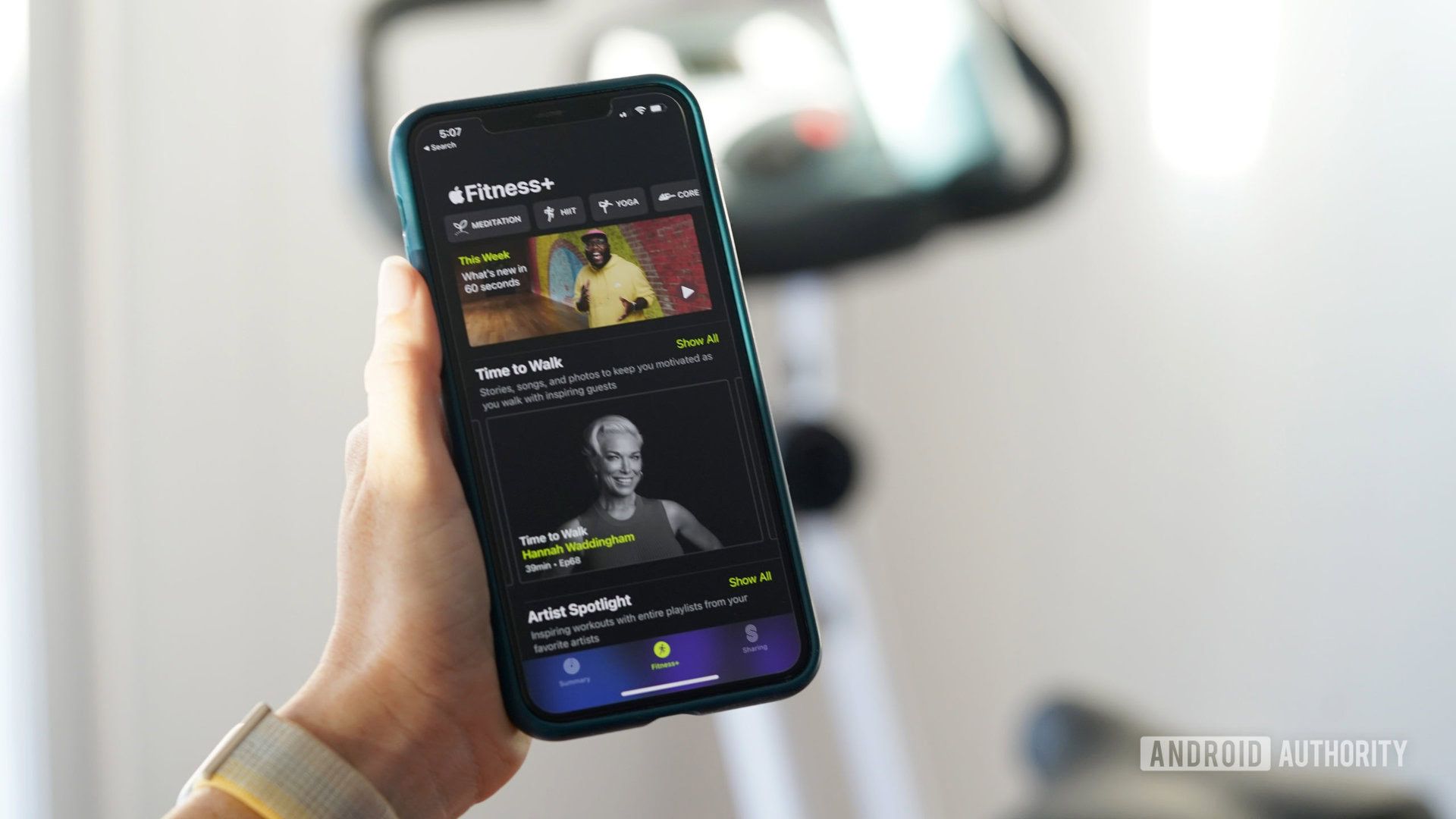 An iPhone in a user's hand displays the Apple Fitness Plus Home Screen.