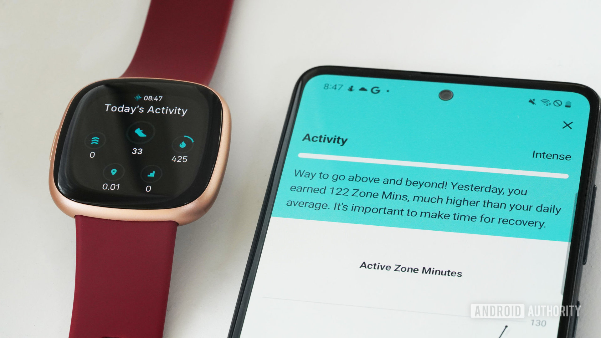 A Galaxy A51 resting alongside a Fitbit Versa 4 displays a users Daily Readiness Score Activity. 