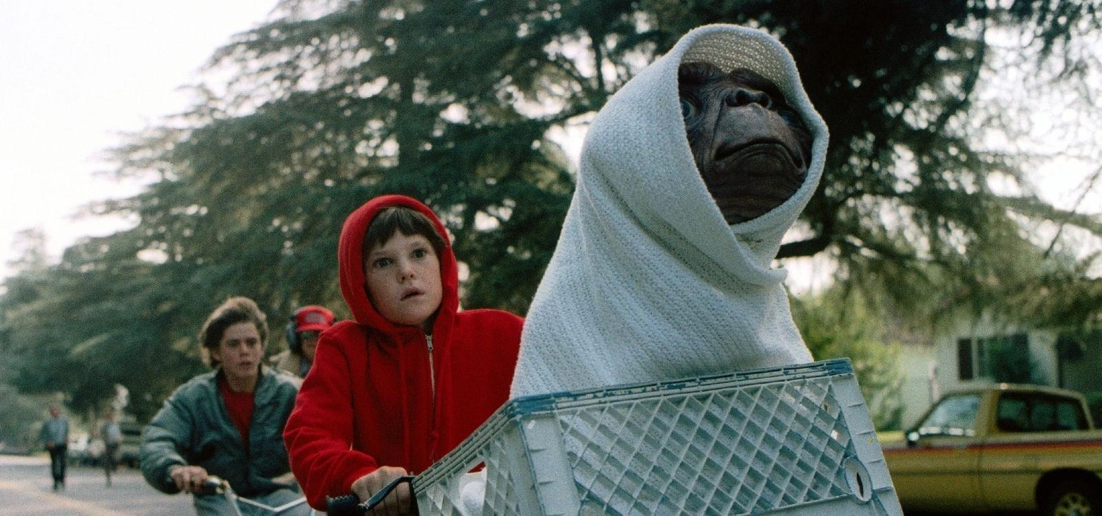 Elliott rides his bike with E.T. covered in a blanket in a bicycle basket - 80s movies