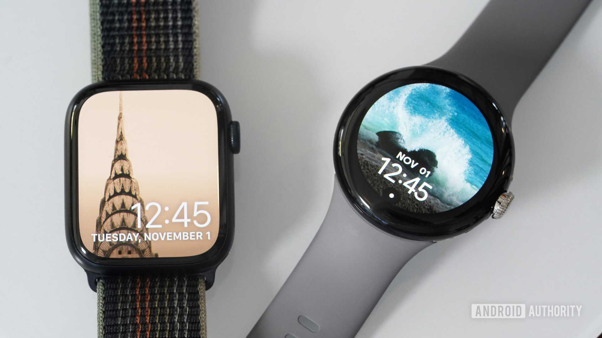 Google Pixel Watch dan Apple Watch Series 8 diletakkan di atas permukaan putih mengkilap, masing-masing menampilkan tampilan jam foto.