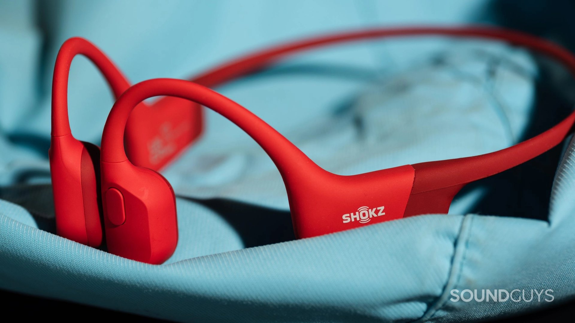 Red Shokz OpenRun headphones lying on a flattened light-blue backpack.