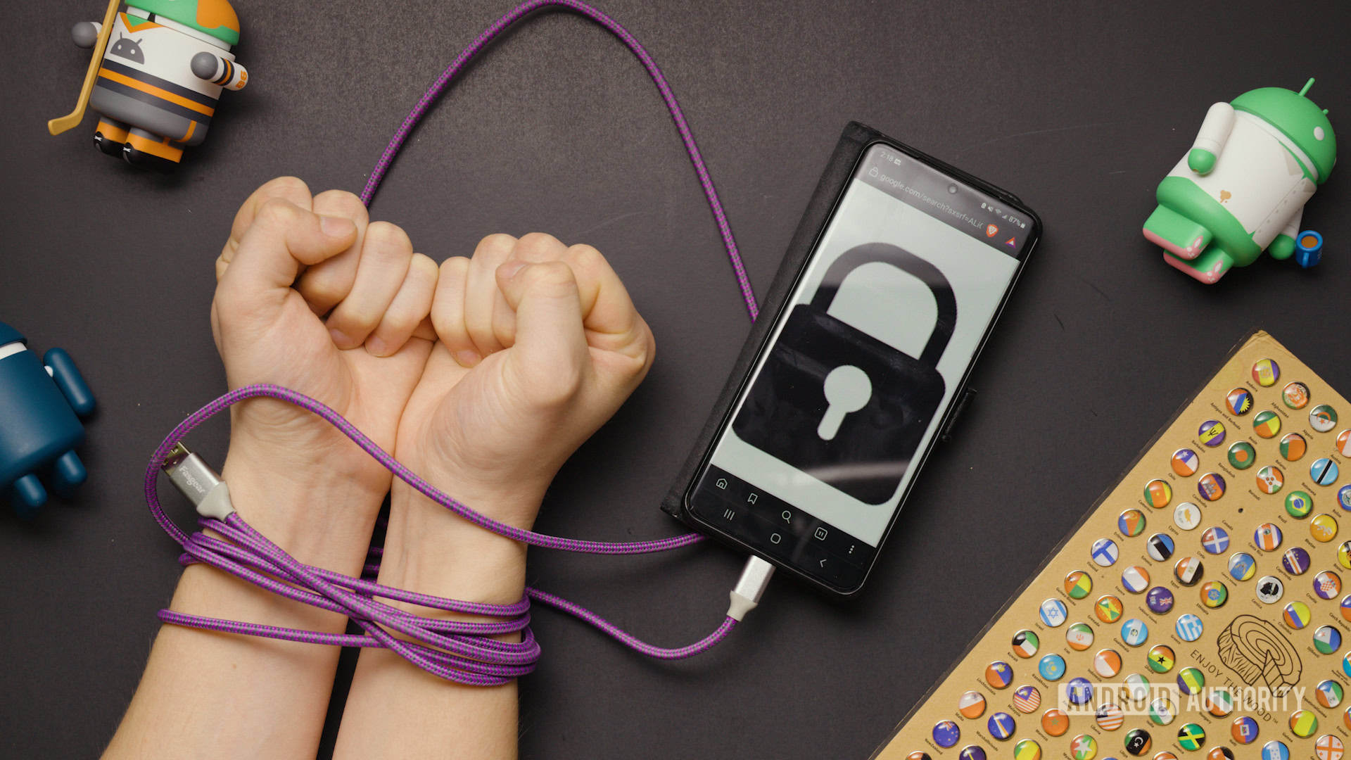 A USB A to USB C cable wrapped around someone's wrists connected to a smartphone with a lock icon shown on its screen.