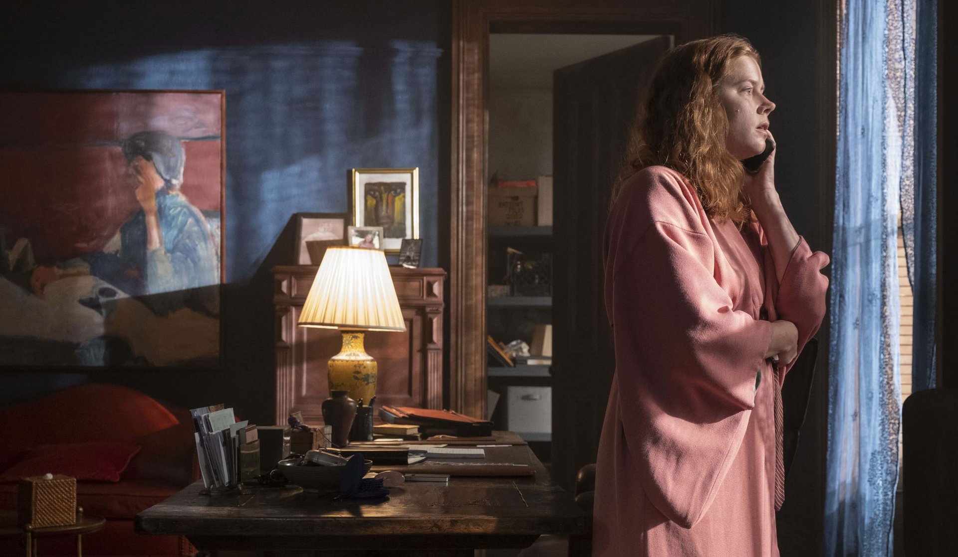 Amy Adams wears a robe and stands in front of her apartment window in Woman in the Window