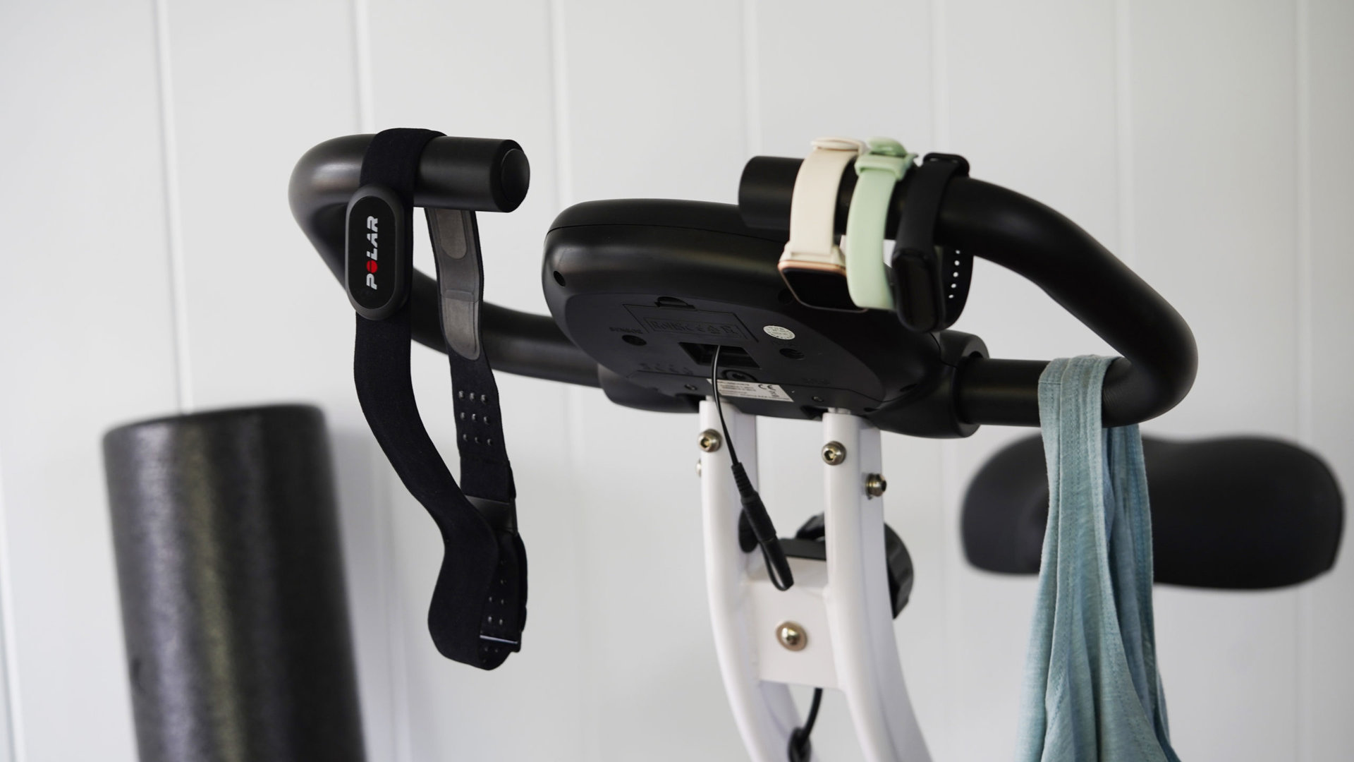 A chest strap and an assortment of review units hang from the handle of a stationary bike. 