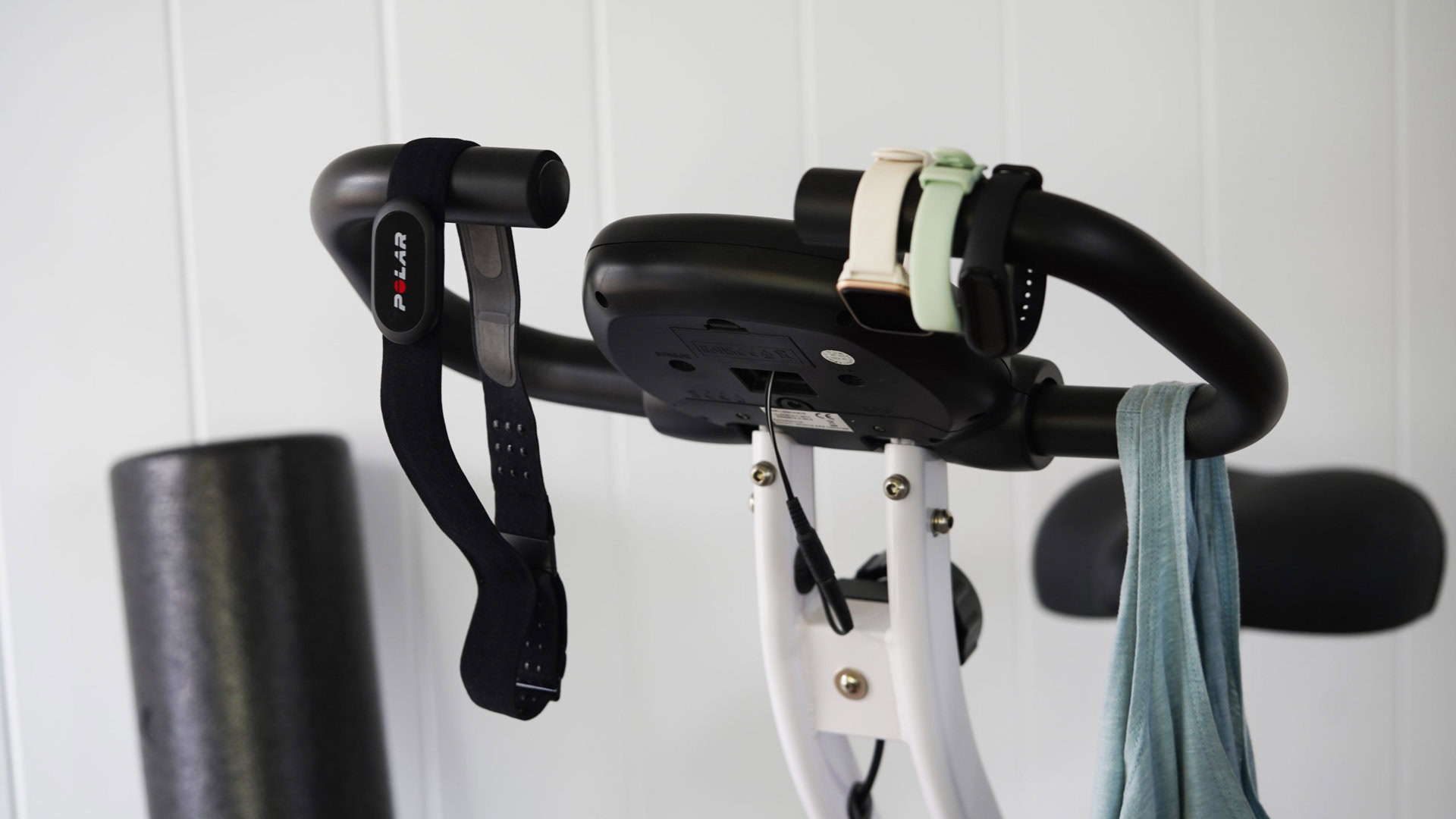 A chest strap and various assessment components hang from the handlebars of a stationary bicycle. 