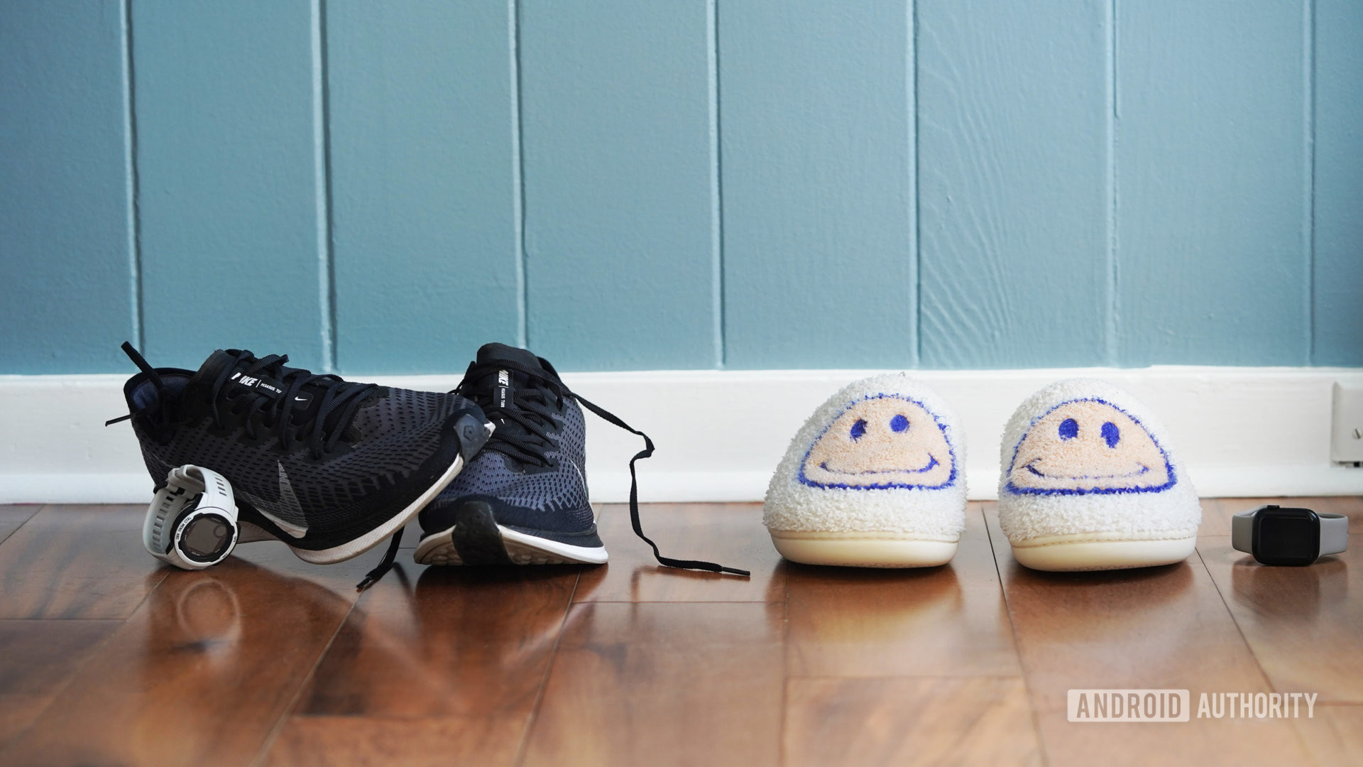 A pair of mens sneakers rest next to a pair of women's slippers.
