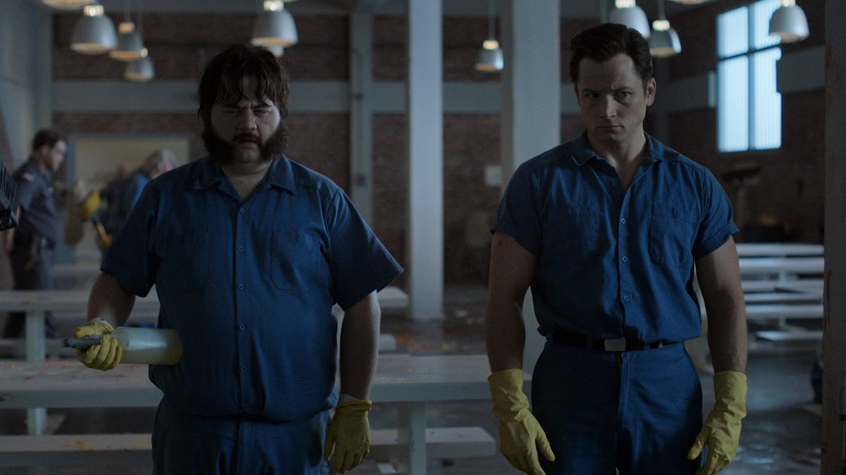 Two prison inmates stand side-by-side wearing rubber gloves in Black Bird