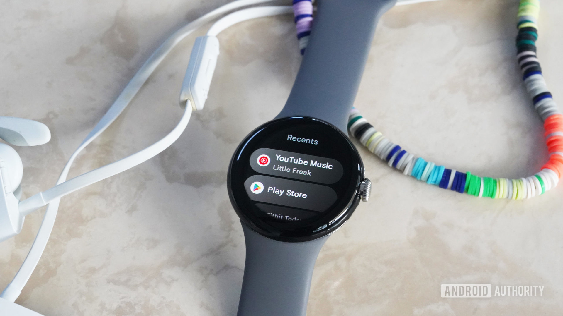 A Pixel Watch rests on a marble table displaying the YouTube Music app.