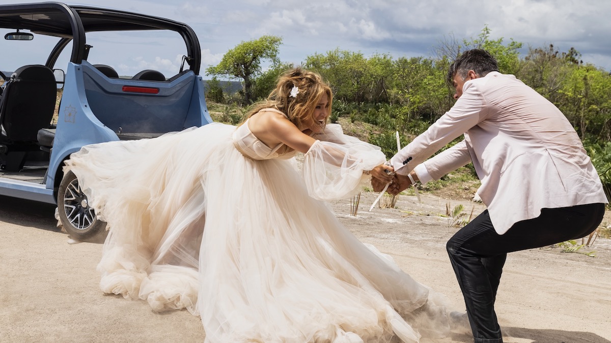 Jennifer Lopez sebagai Darcy Rivera dalam gaun pengantin, mengenakan kerudungnya.  Ujung lainnya ditarik oleh osh Duhamel sebagai Tom Fowler di Shotgun Wedding - streaming film tahun 2023