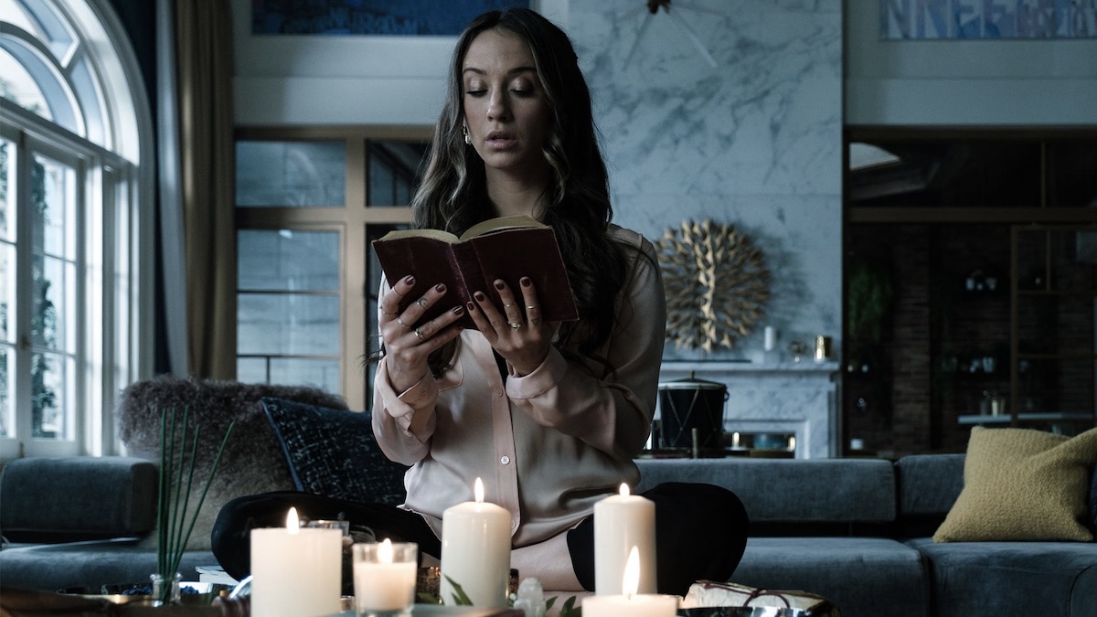 Seorang wanita membaca dari sebuah buku kuno yang dikelilingi oleh lilin di The Magicians - menunjukkan seperti bahan gelapnya