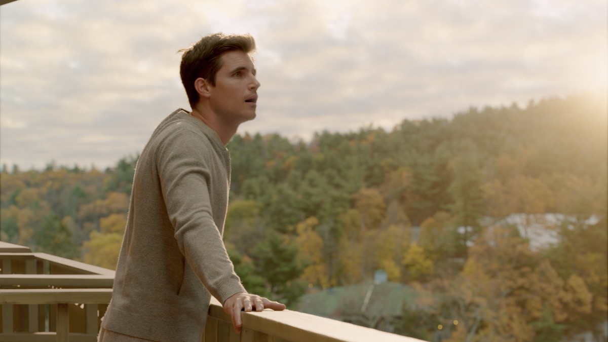 A man stands on a balcony looking out at a forest in Upload